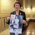 Egea Haffner con la locandina delle iniziative della Città per il Giorno del Ricordo, che riporta la sua foto da bambina con la valigia
